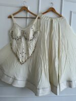 Off-white cream rayon cotton chaniya choli on hangers showing 6-meter flair skirt with mirror lace and padded stitched blouse with authentic hand-stitched sea shells and mirror embellishments.